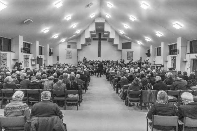A view from the back of the church towards the east end, showing a packed audience and the orchestra and conductor ready to start their performance