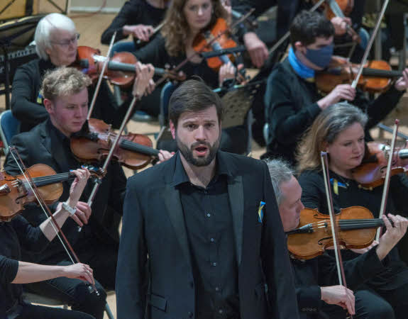 A closeup of Gareth Brynmor John with the first violins behind him