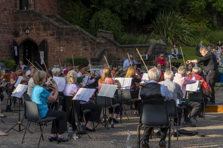 John Moore conducting the orchestra, viewed from behind the first violins towards the cellos